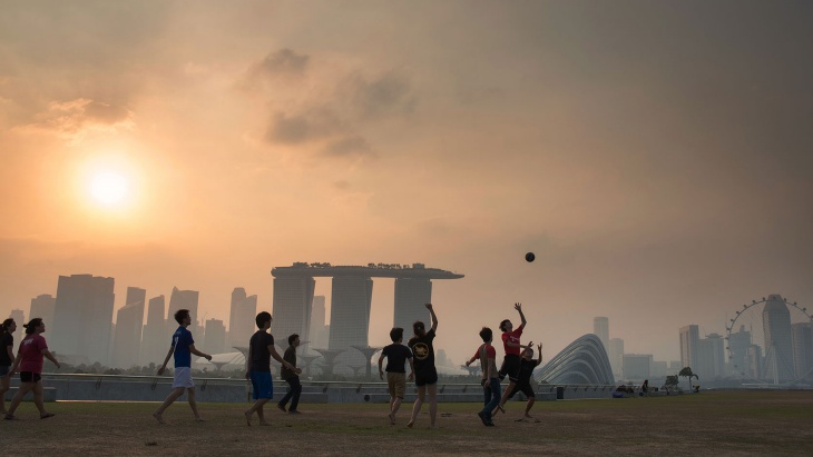 dusk，A group of boys on the marina embankment (Marina Barrage) play football，In the distance is the hazy silhouette of Marina Bay