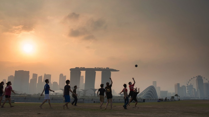 黄昏时分，一群男孩在滨海堤坝 (Marina Barrage) 上踢足球，远处是滨海湾的朦胧轮廓